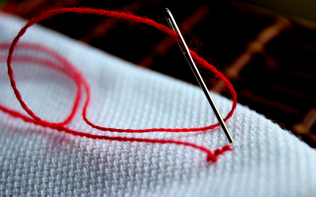 Needle and thread stitching into white fabric, single patch order